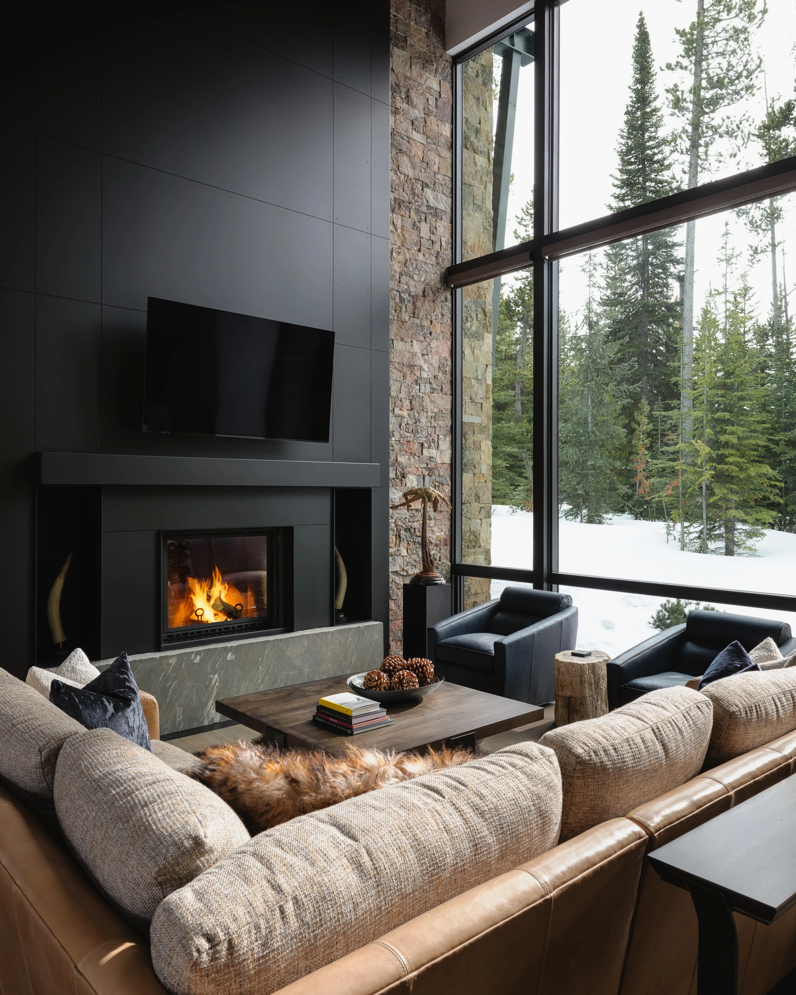 Living room fireplace framed by a floor-to-ceiling window onto snow-covered pines — interior design photography Big Sky Montana, Reid Smith Architects